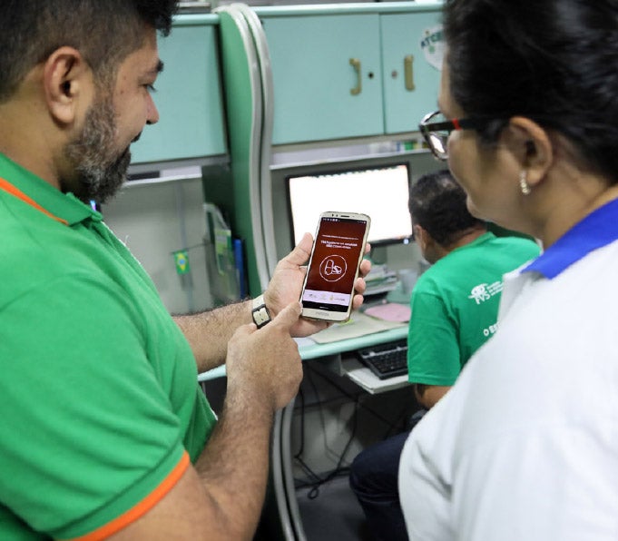 Un hombre le muestra a un trabajador de la salud cómo usar una aplicación de teléfono.