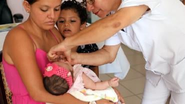 Mother holds baby in her arms while nurse vaccinates her