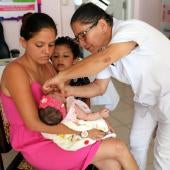 Mother holds baby in her arms while nurse vaccinates her