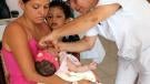 Mother holds baby in her arms while nurse vaccinates her
